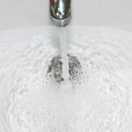 Zatkany odpływ w umywalce podczas próby spłynięcia wody – widoczny zastój i problem z drożnością rury.